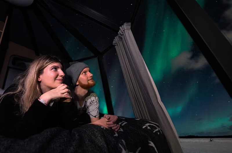 Couple watching the Northern Lights from the inside of an Aurora Nest igloo