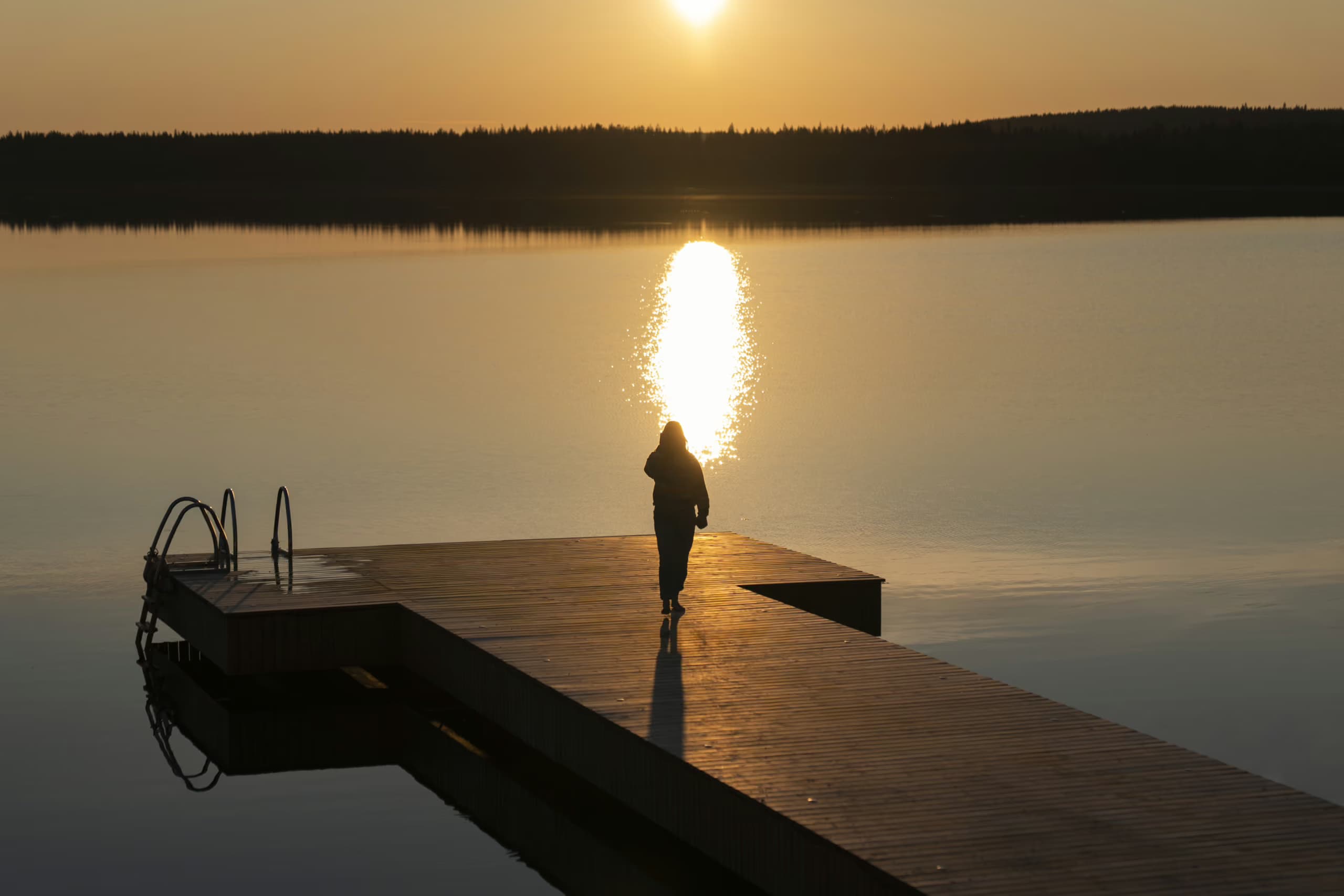 Woman on a pier admiring a sunset at Lake Palojärvi