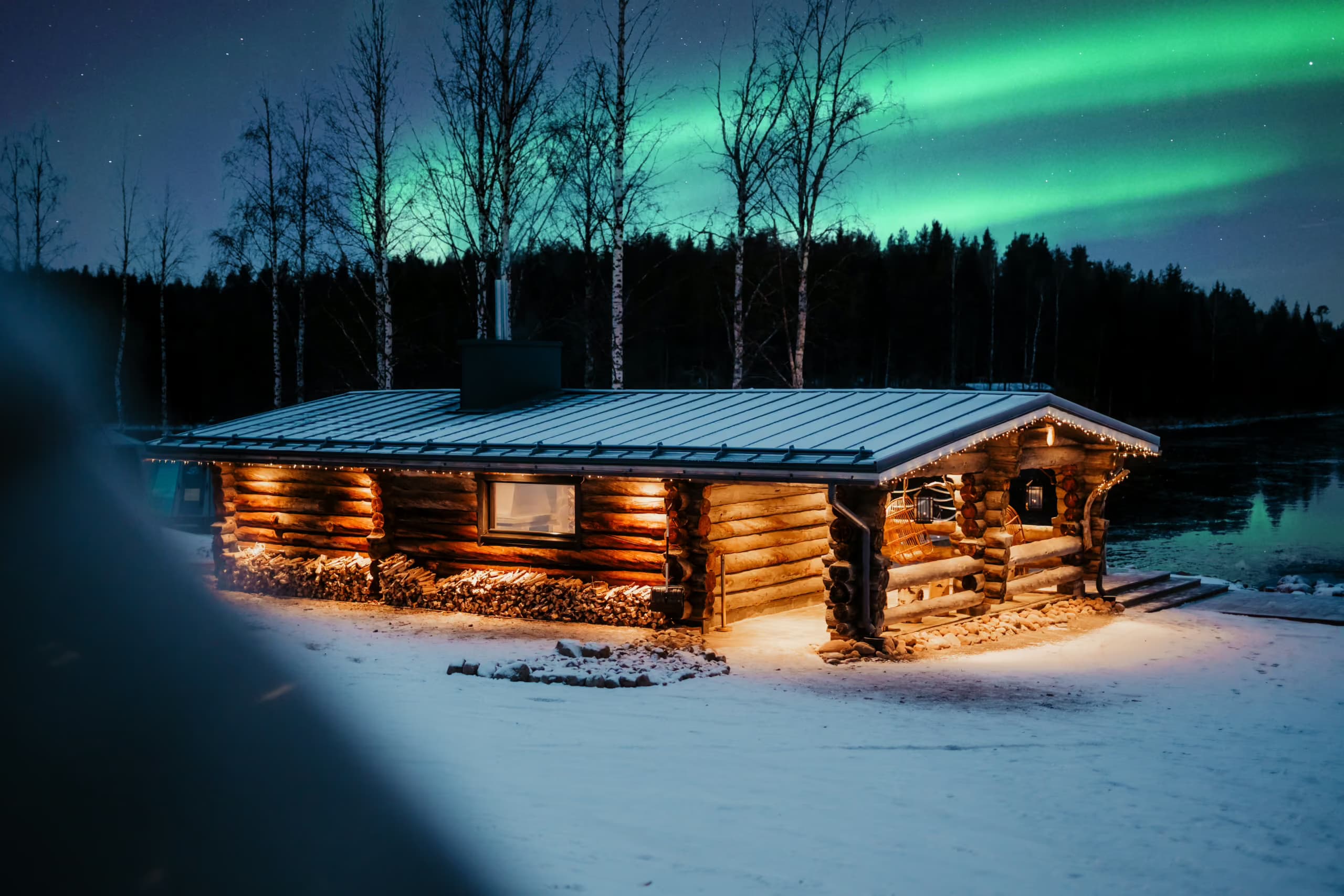 Lakeside sauna building at Aito Resort illuminated at night with Northern Lights