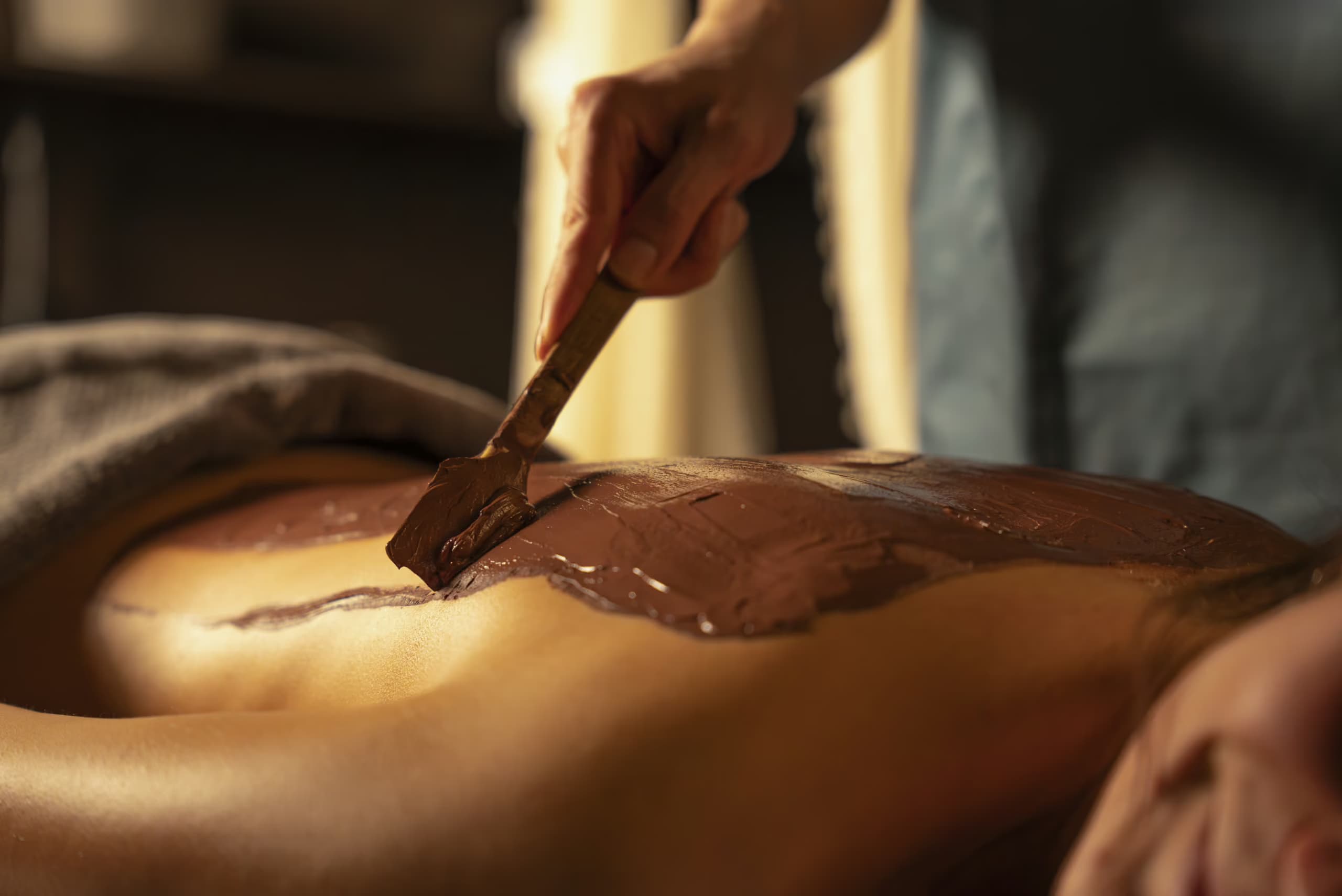 Spa therapist applying a mud treatment on a woman’s back at Aito Resort